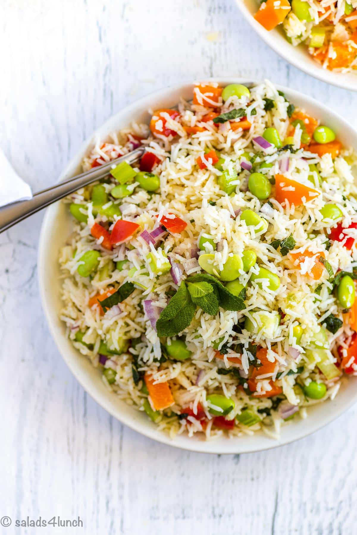 Close up of basmati rice salad with peppers, celery, mint and edamame on a white plate.