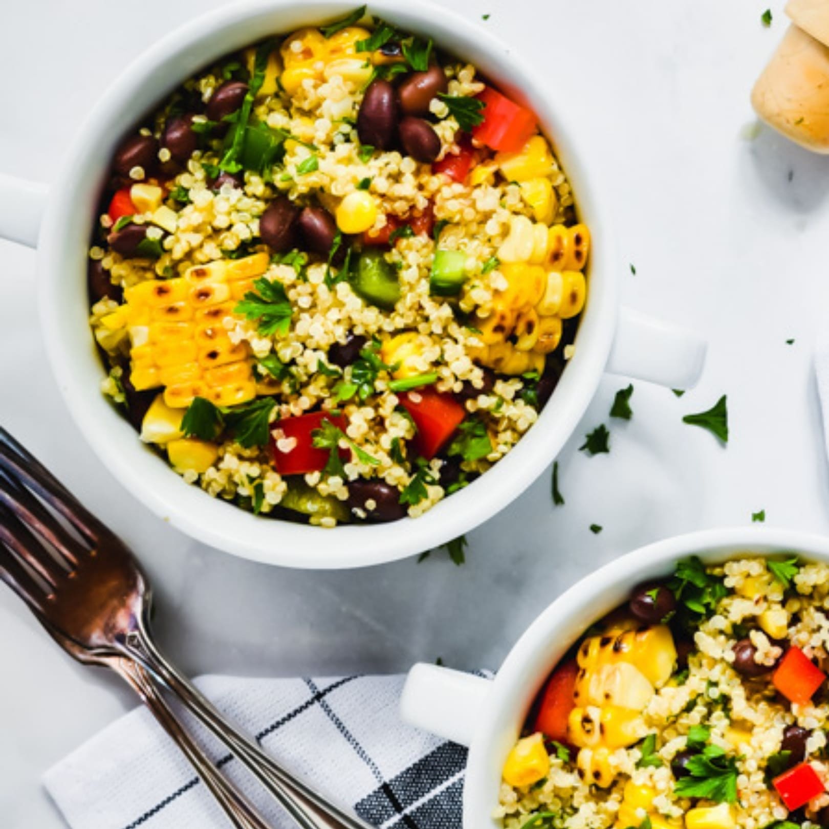 Close up of Corn and Black Bean Salad in a white bowl on a white table with a silver fork.