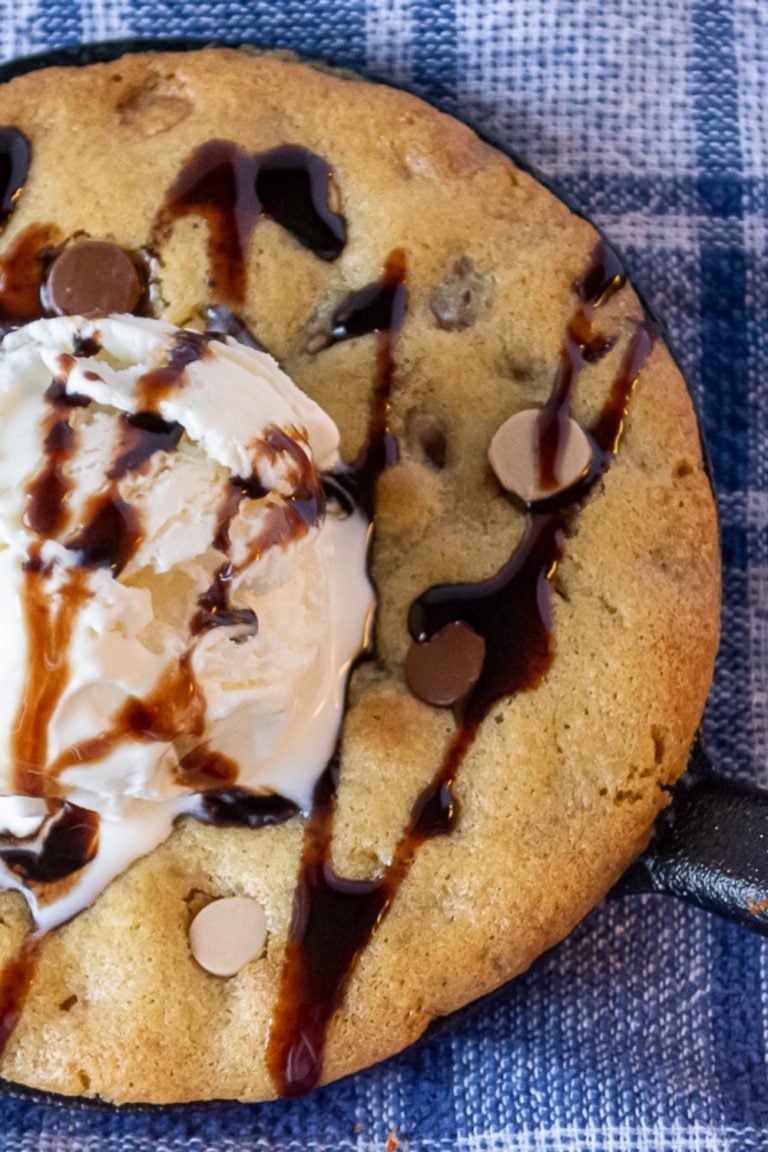 Close up of Salted Caramel and Chocolate Chip SKillet Cookie topped with vanilla ice cream and drizzled with chocolate on a blue and white plaid napkin.